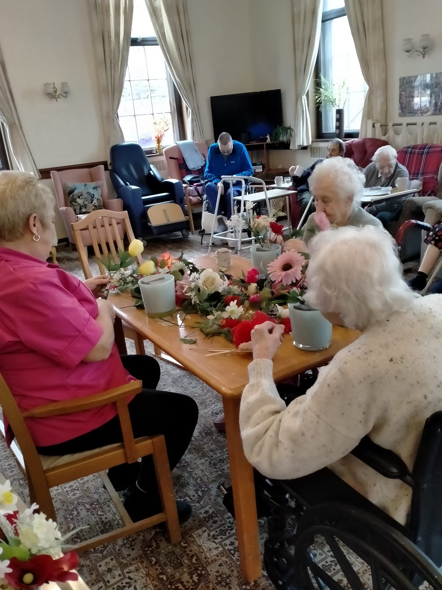A group of elderly people are sitting around a table in a living room.