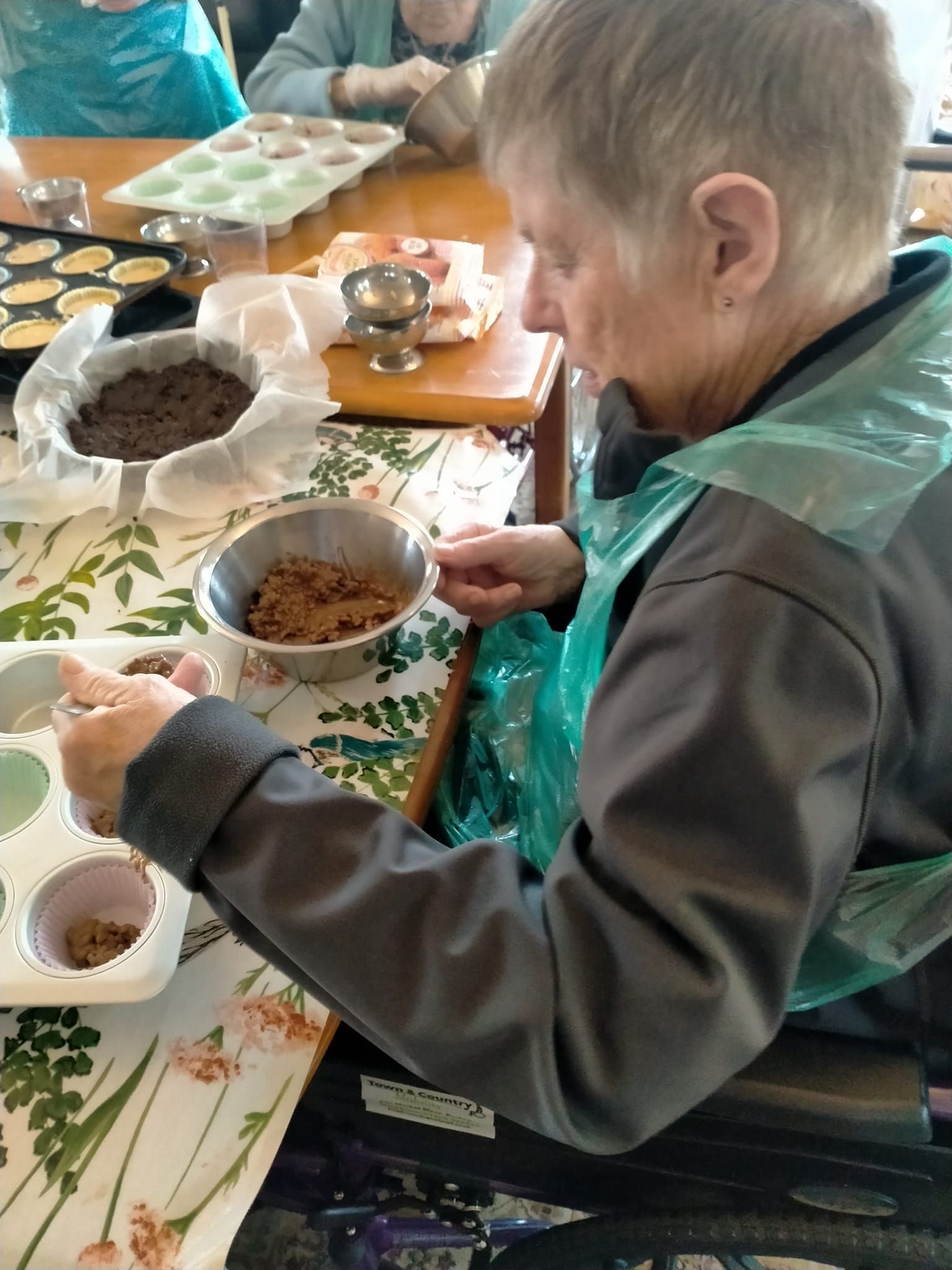 An elderly woman is sitting at a table mixing ingredients in a bowl.