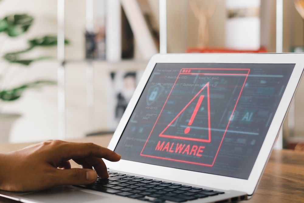 Laptop displaying a malware warning on-screen; a person's hand is on the keyboard.