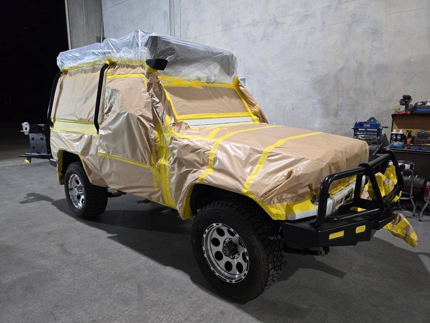 A jeep is covered in yellow tape and is sitting in a garage.