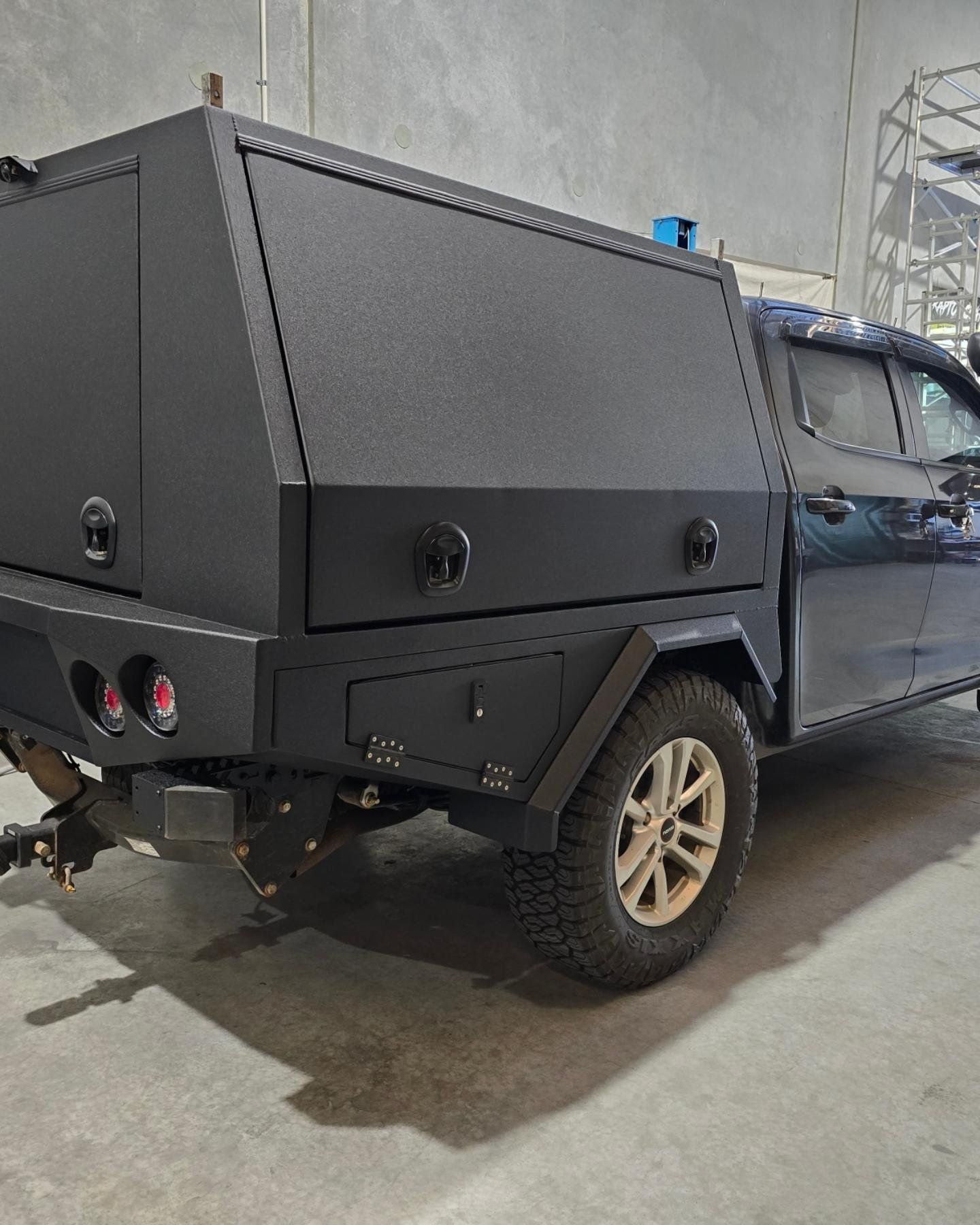 A black truck with a black canopy is parked in a warehouse.