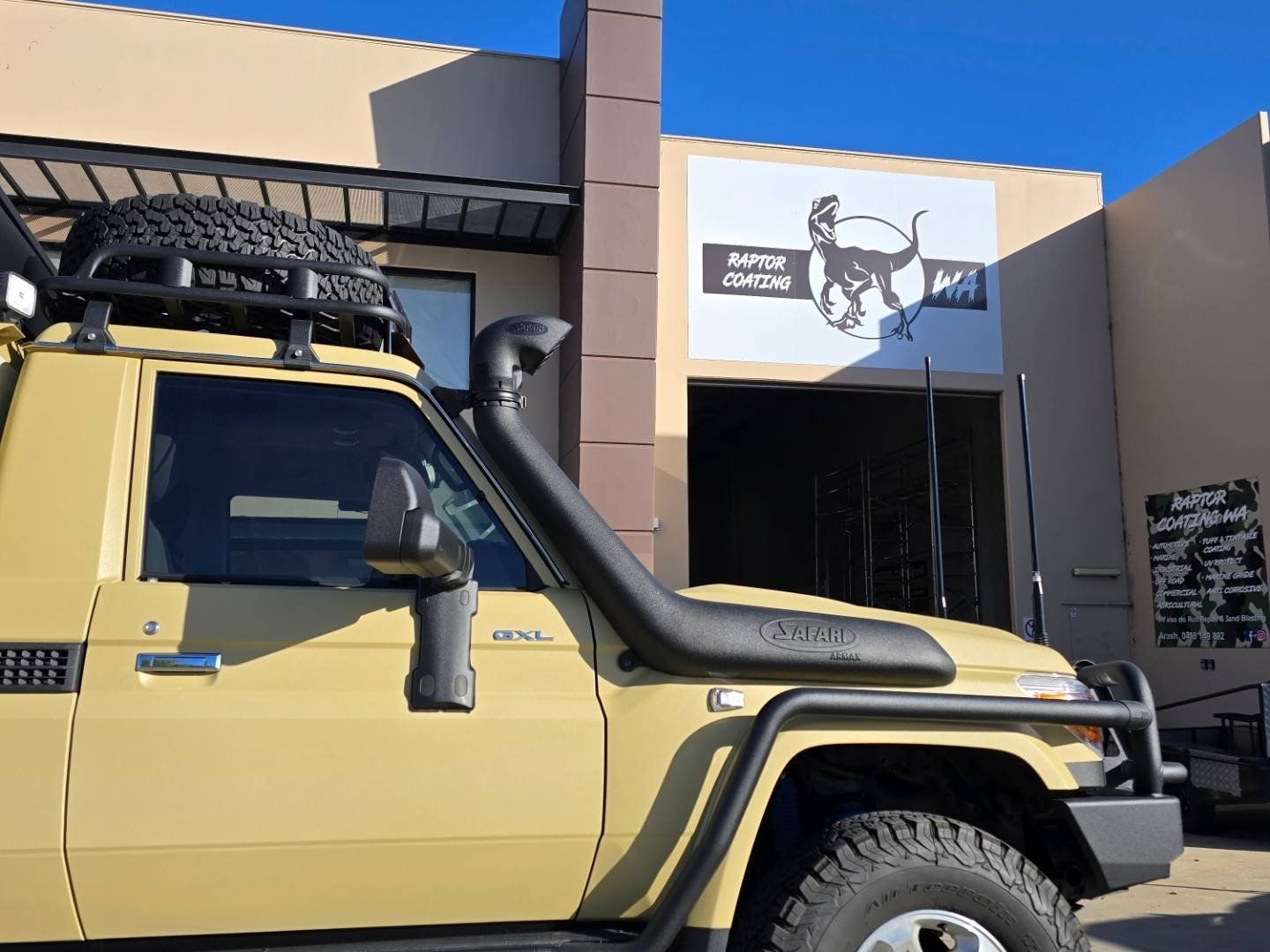 A yellow truck with a snorkel on the hood is parked in front of a building.