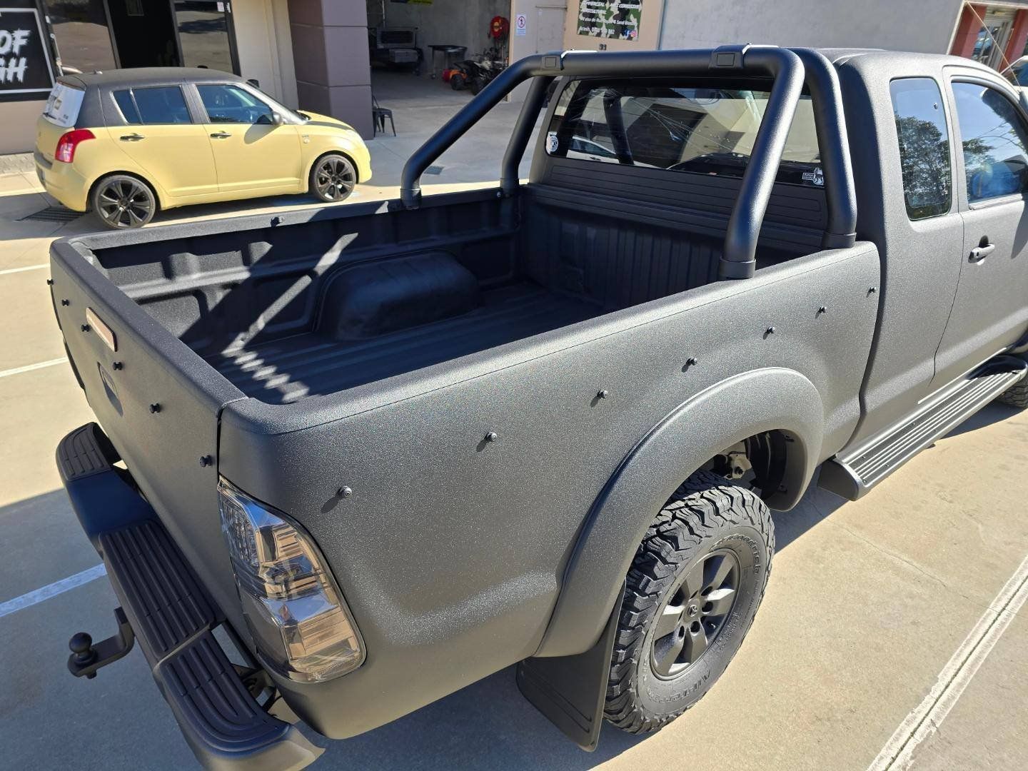 A black truck is parked in a parking lot next to a yellow car.