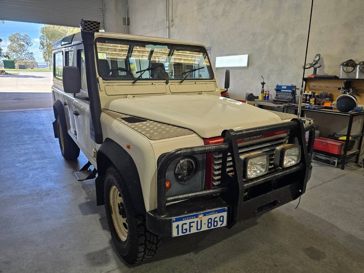 A white land rover defender is parked in a garage.