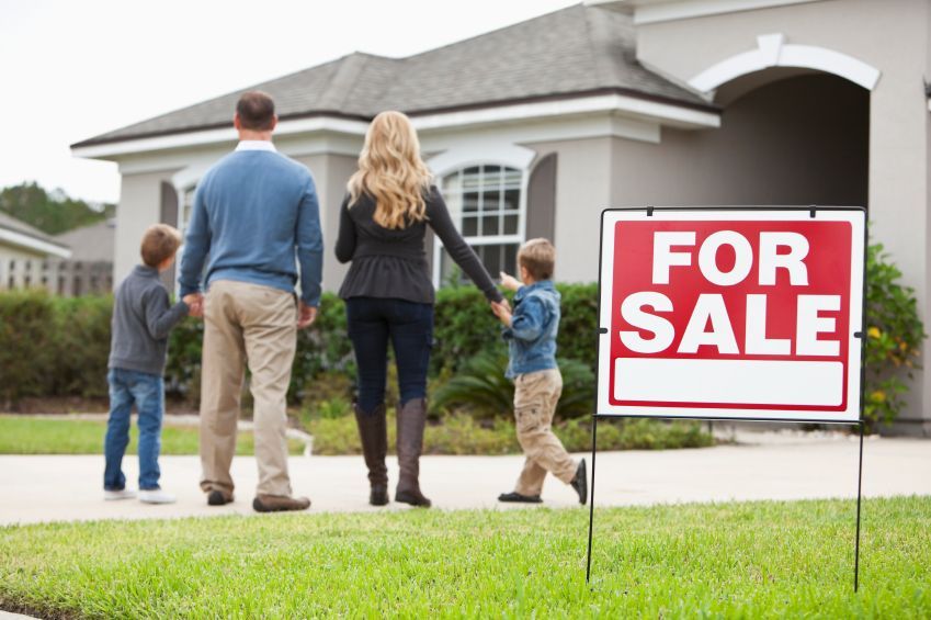 A family standing in front of a house with a for sale sign