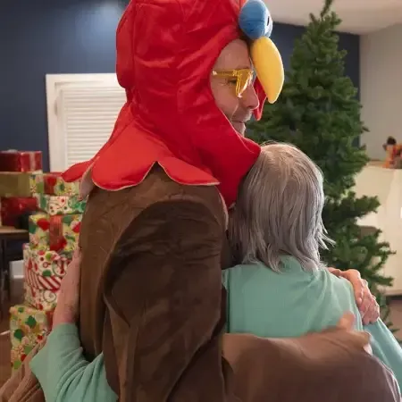a man in a parrot costume is hugging a woman in front of a christmas tree