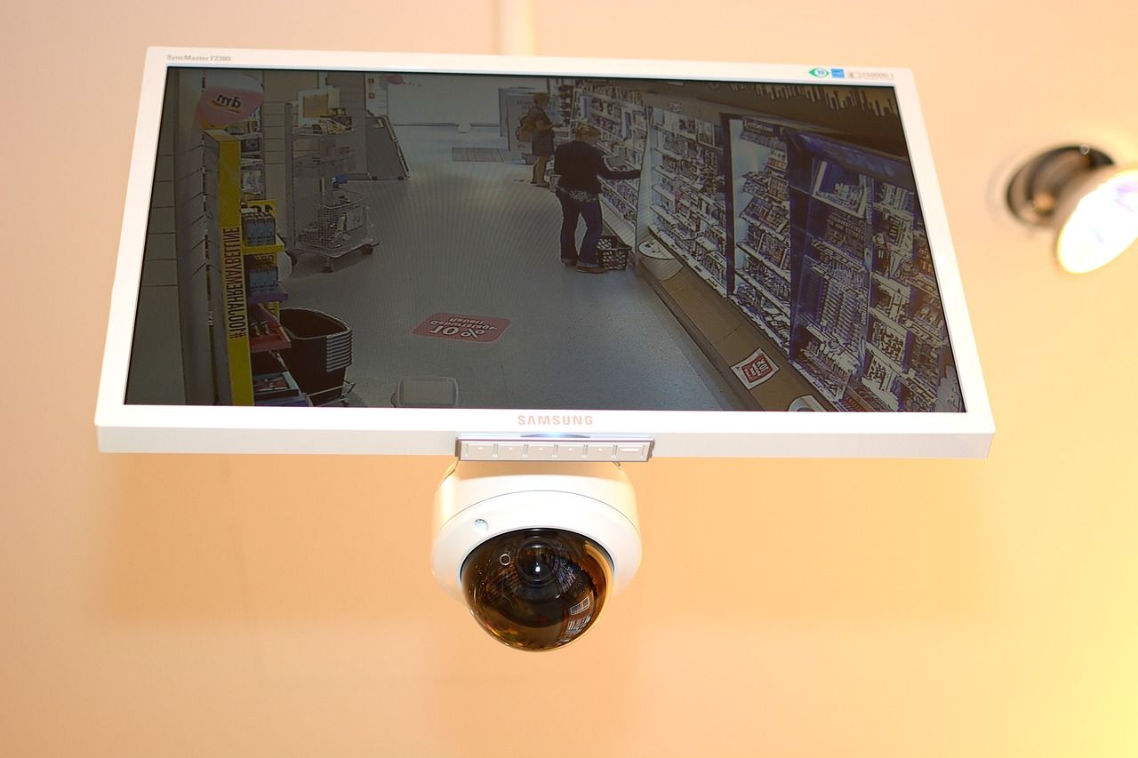A security camera is hanging from the ceiling above a monitor.