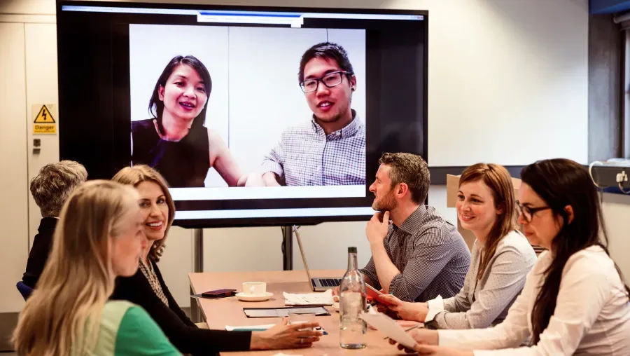 A group of people are sitting around a table in front of a large screen.
