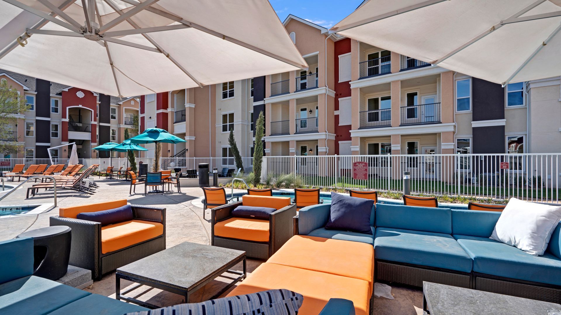 A patio area with couches , chairs , tables and umbrellas in front of a building.
