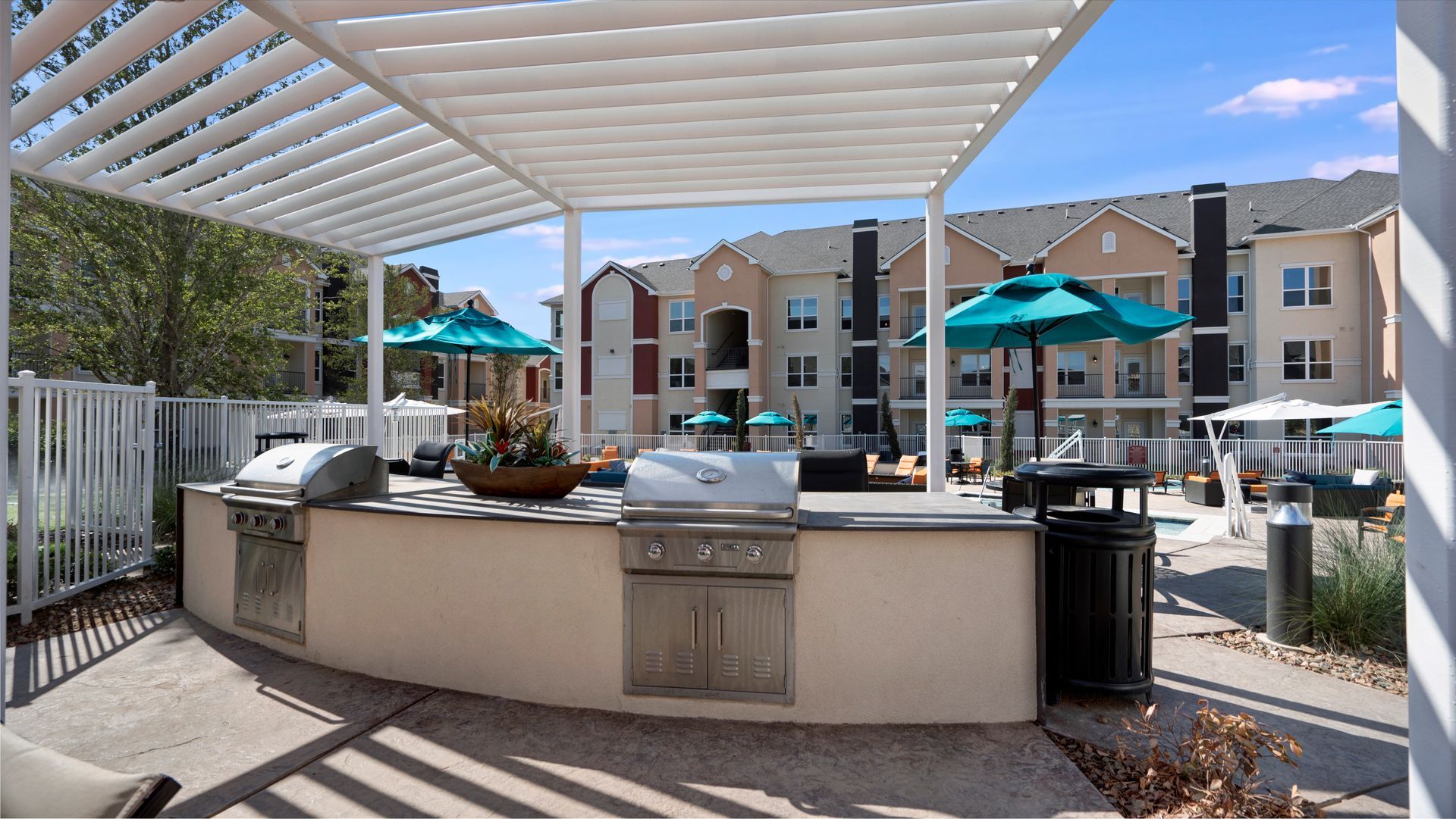 A large outdoor kitchen with a grill and umbrellas under a pergola.