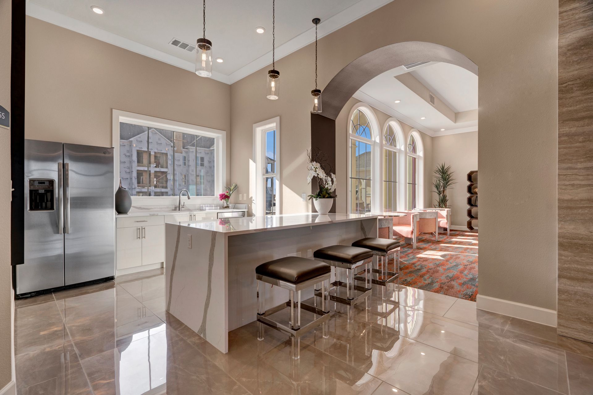 A kitchen with a large island , stools and a refrigerator.