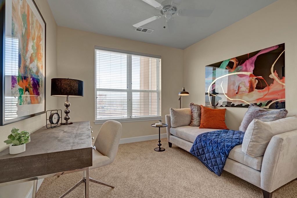 A living room with a couch , desk , chair and a painting on the wall.