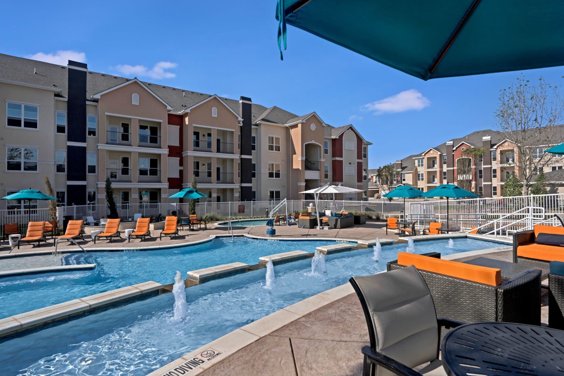 A large swimming pool surrounded by chairs and umbrellas in front of a building.