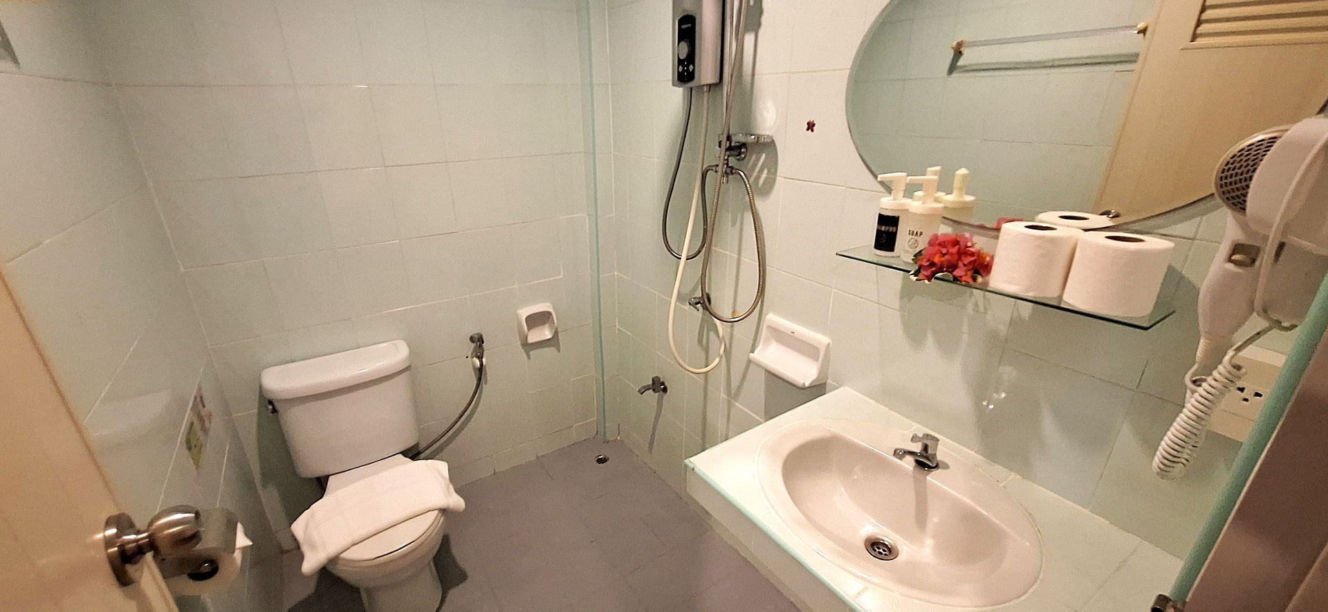 A small, light blue bathroom featuring a toilet with a towel, sink, mirror, and shower fixtures.