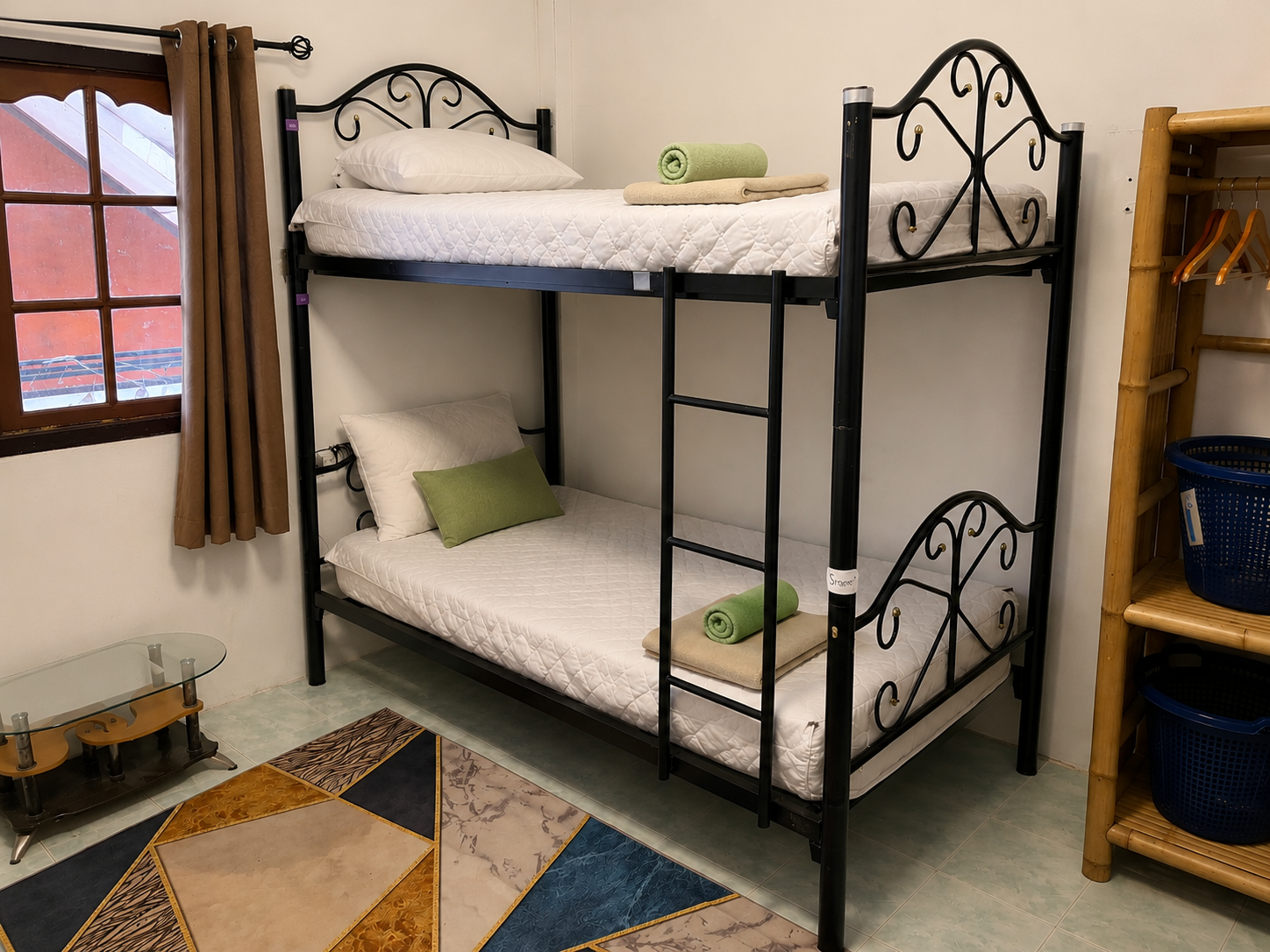 Bunk bed with black metal frame in a small bedroom, beside a window and a wooden shelf.
