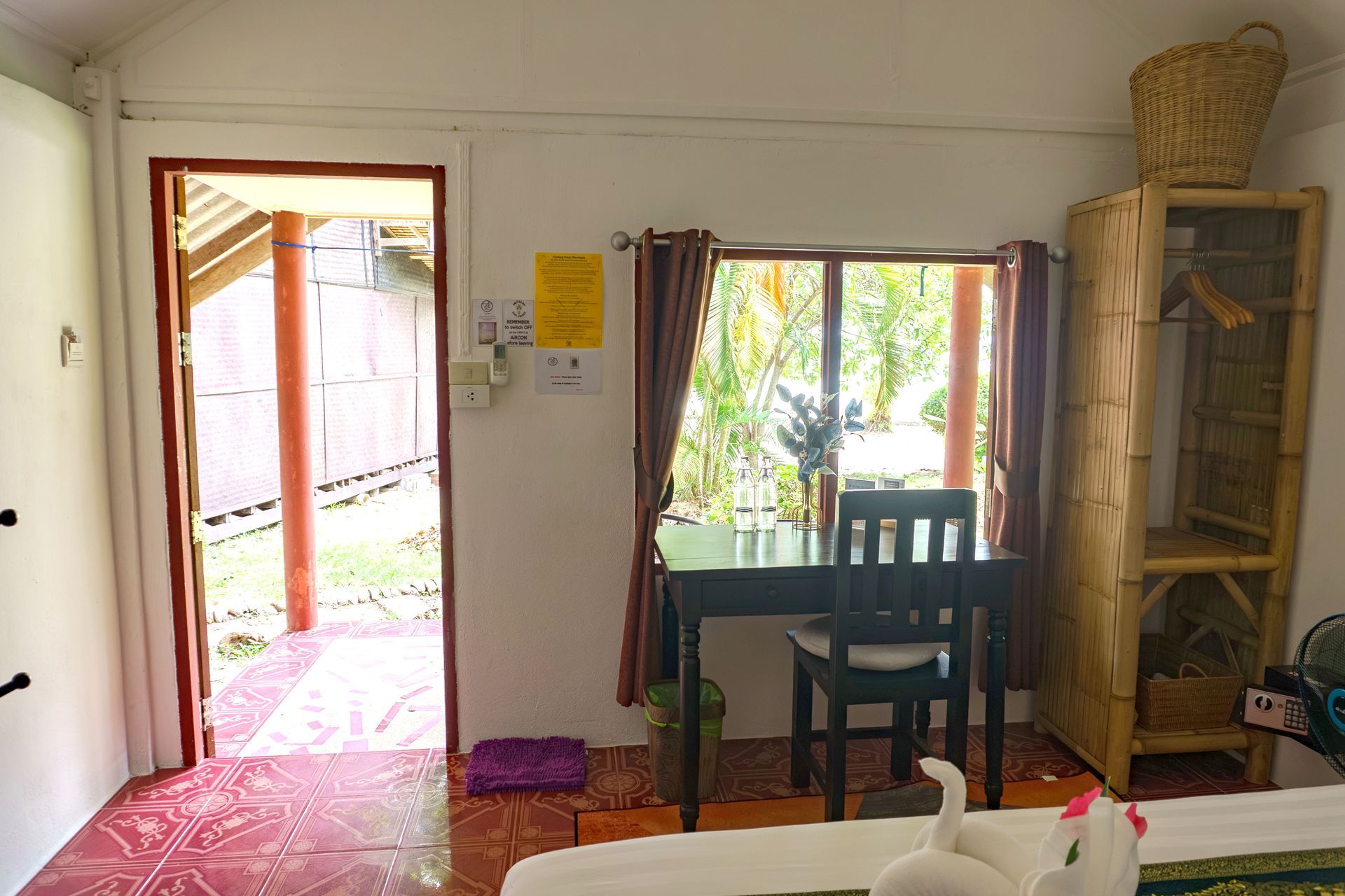 Interior of a small room with open door, desk, bamboo shelving, and window with outdoor view.