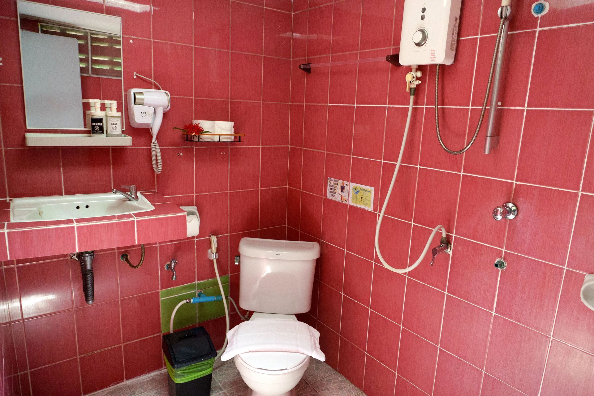 Red tiled bathroom with a toilet, sink, mirror, and shower fixtures.