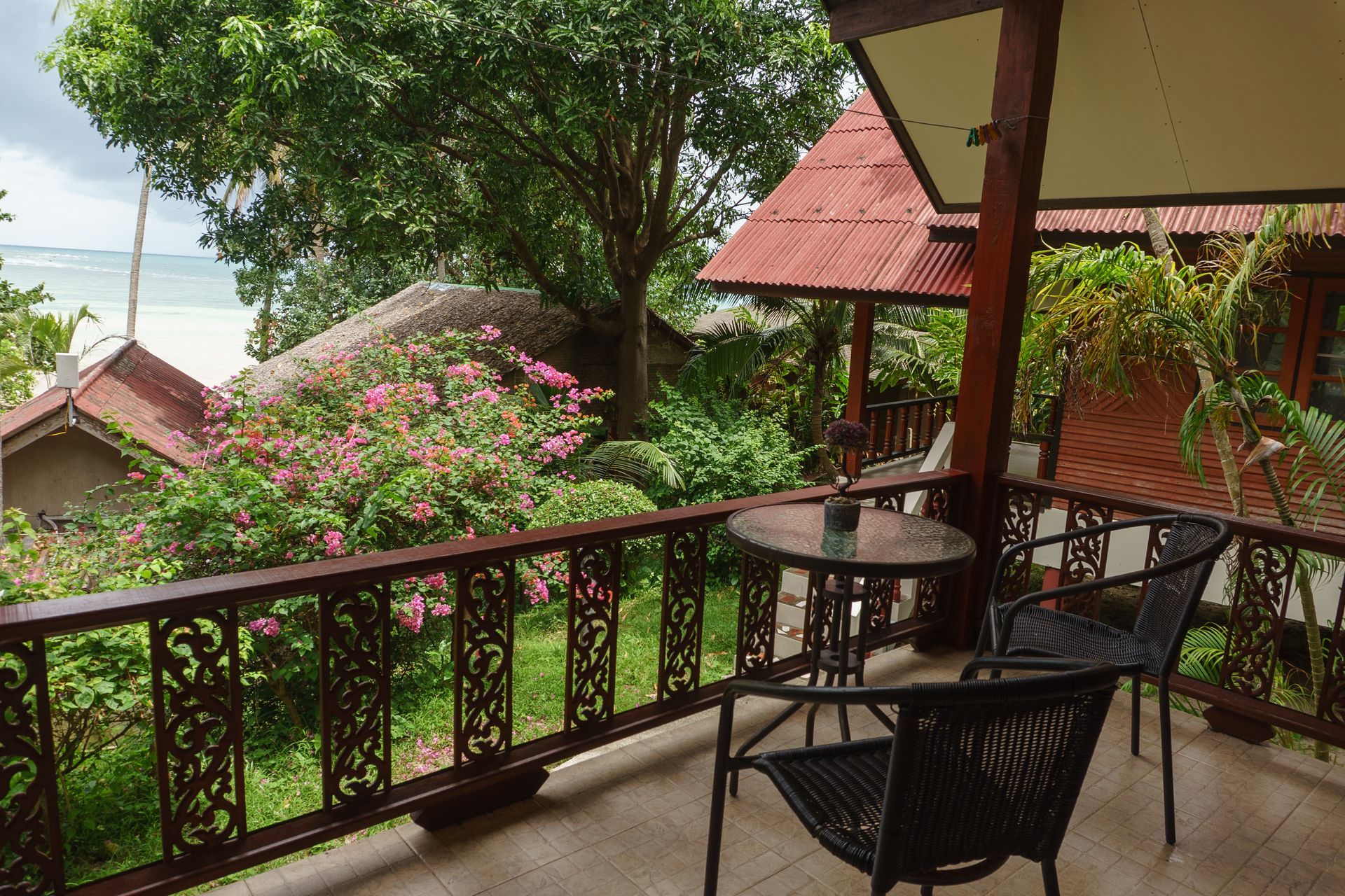 Balcony with table, chairs, lush plants, and ocean view.