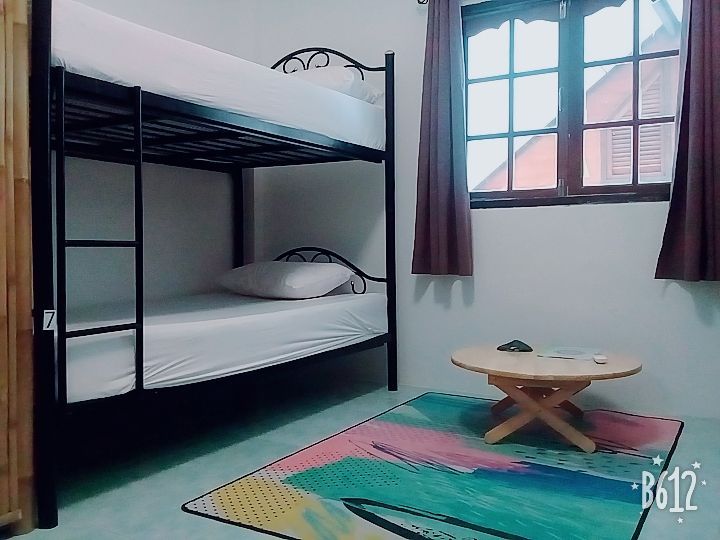 Bunk bed in a room with a window, rug, and small table. White bedding, dark metal frame.