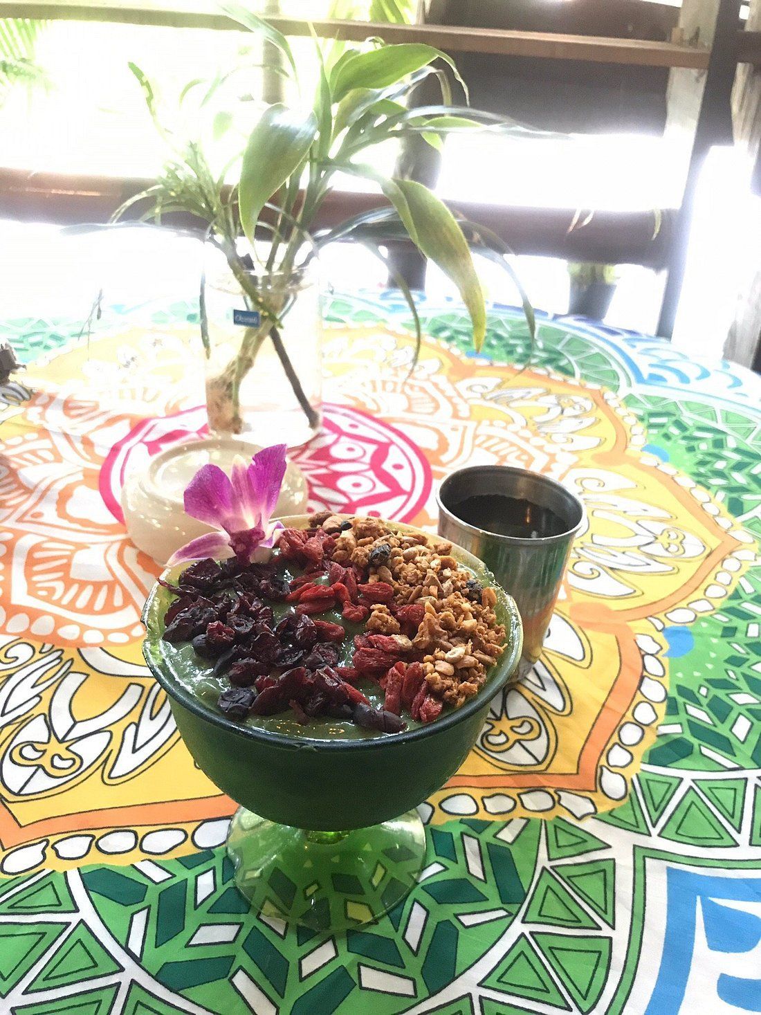 Green smoothie bowl topped with berries and granola on a colorful table; a glass of water nearby.