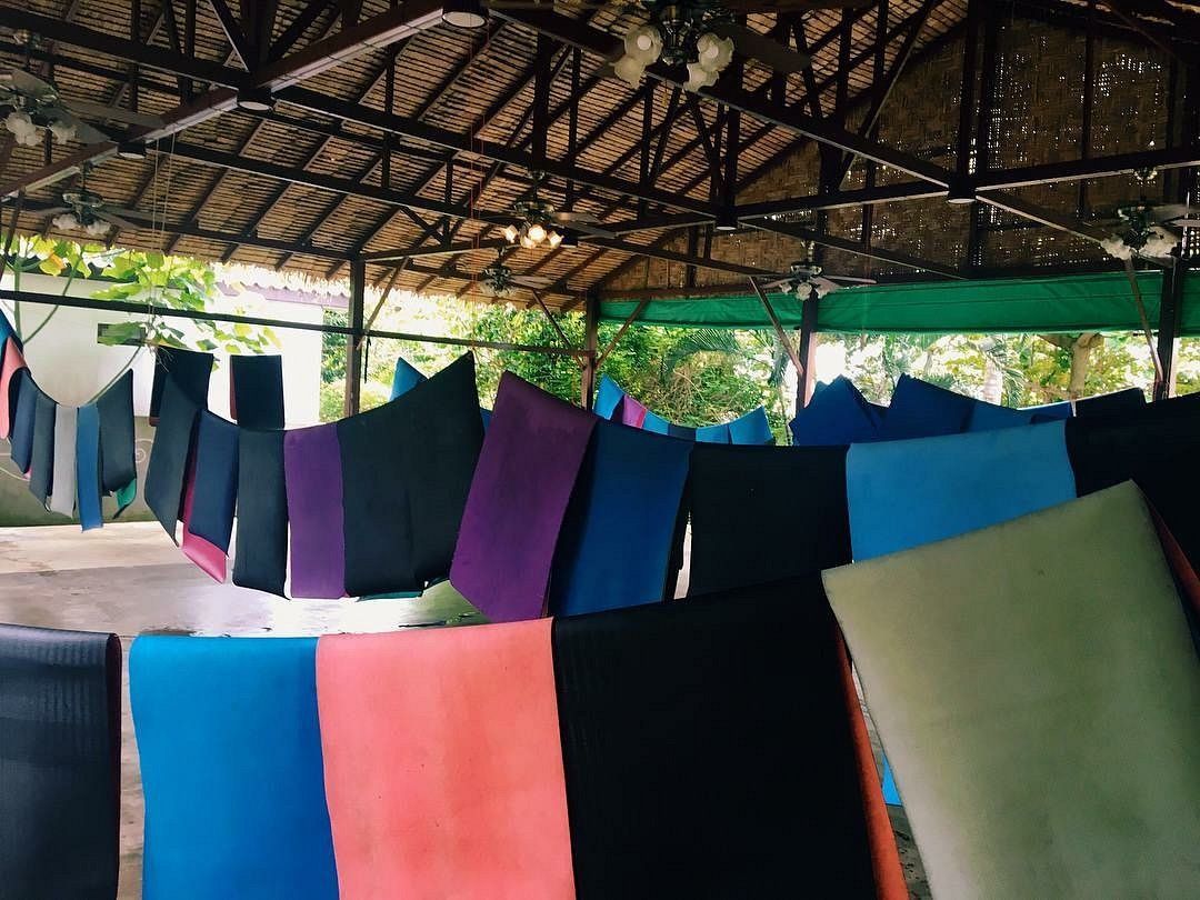 Colorful yoga mats hanging out to dry under a thatched roof.