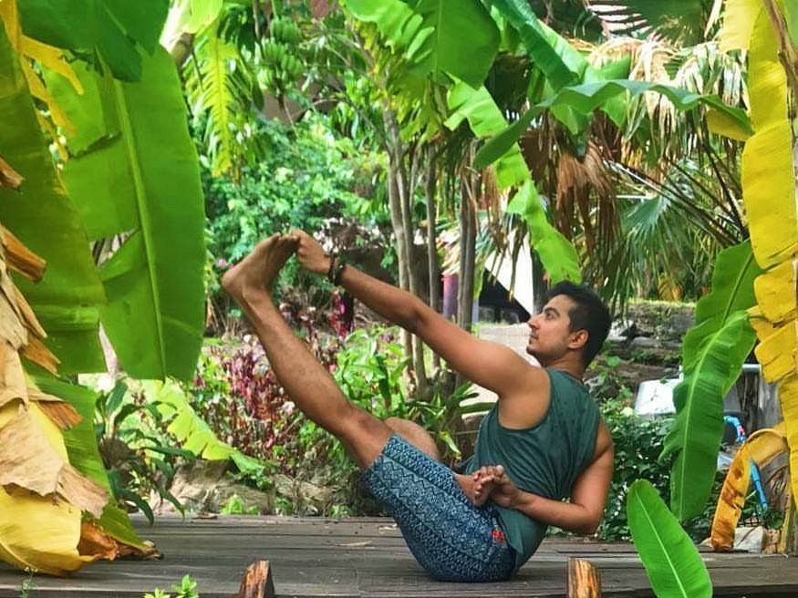 Man in yoga pose outdoors, surrounded by green tropical plants.