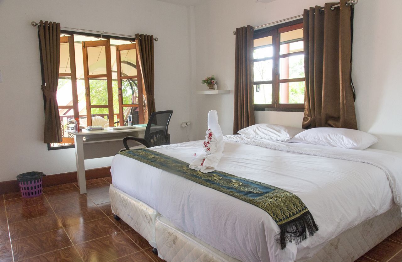 Bedroom with white bed, desk, open window, brown curtains, and a bird-shaped towel.