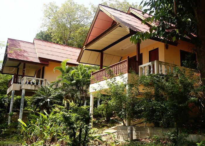 Two yellow cabins with red-tiled roofs, surrounded by lush green foliage, in a tropical setting.