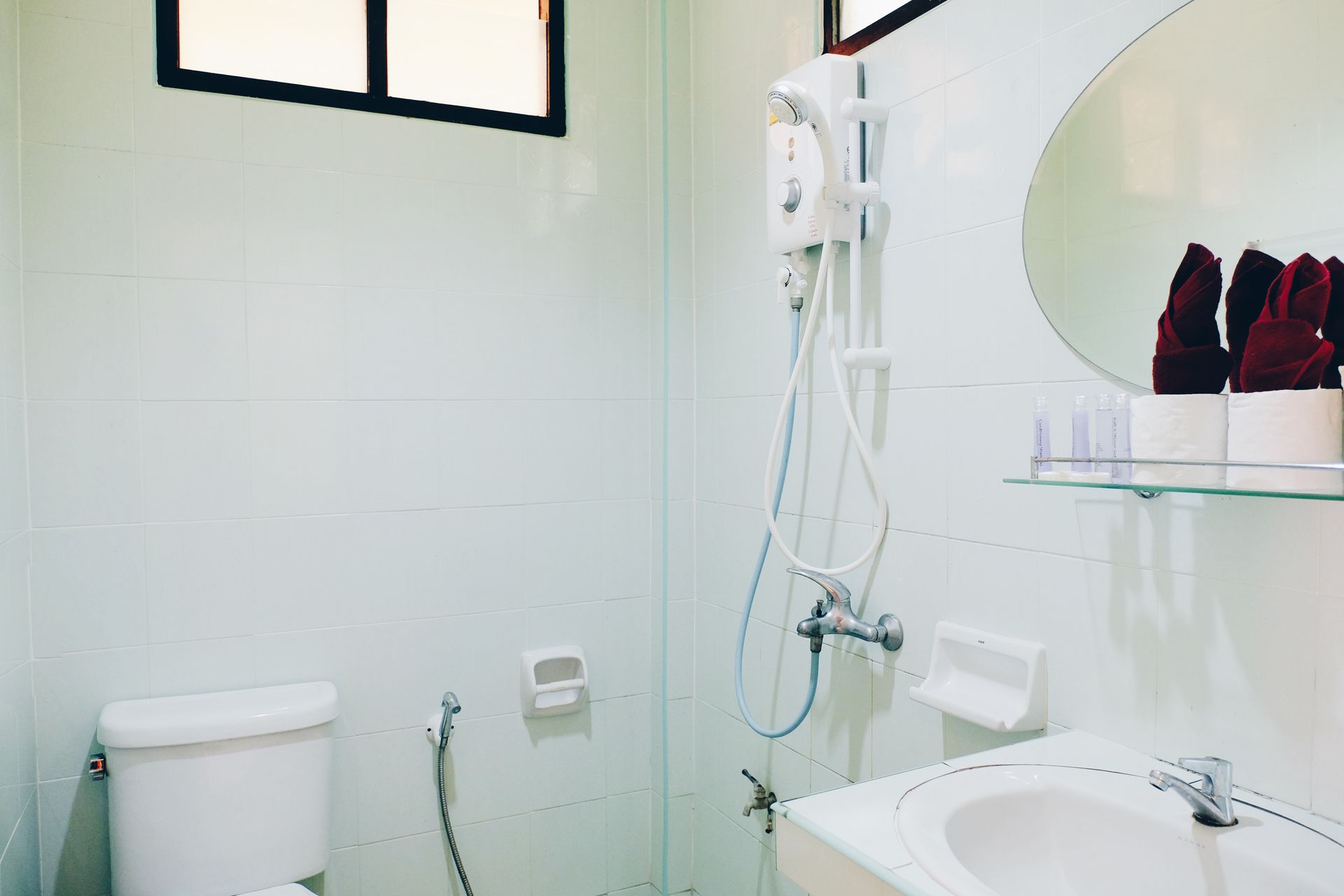 Small, white bathroom with toilet, sink, shower, and a mirror with towels.