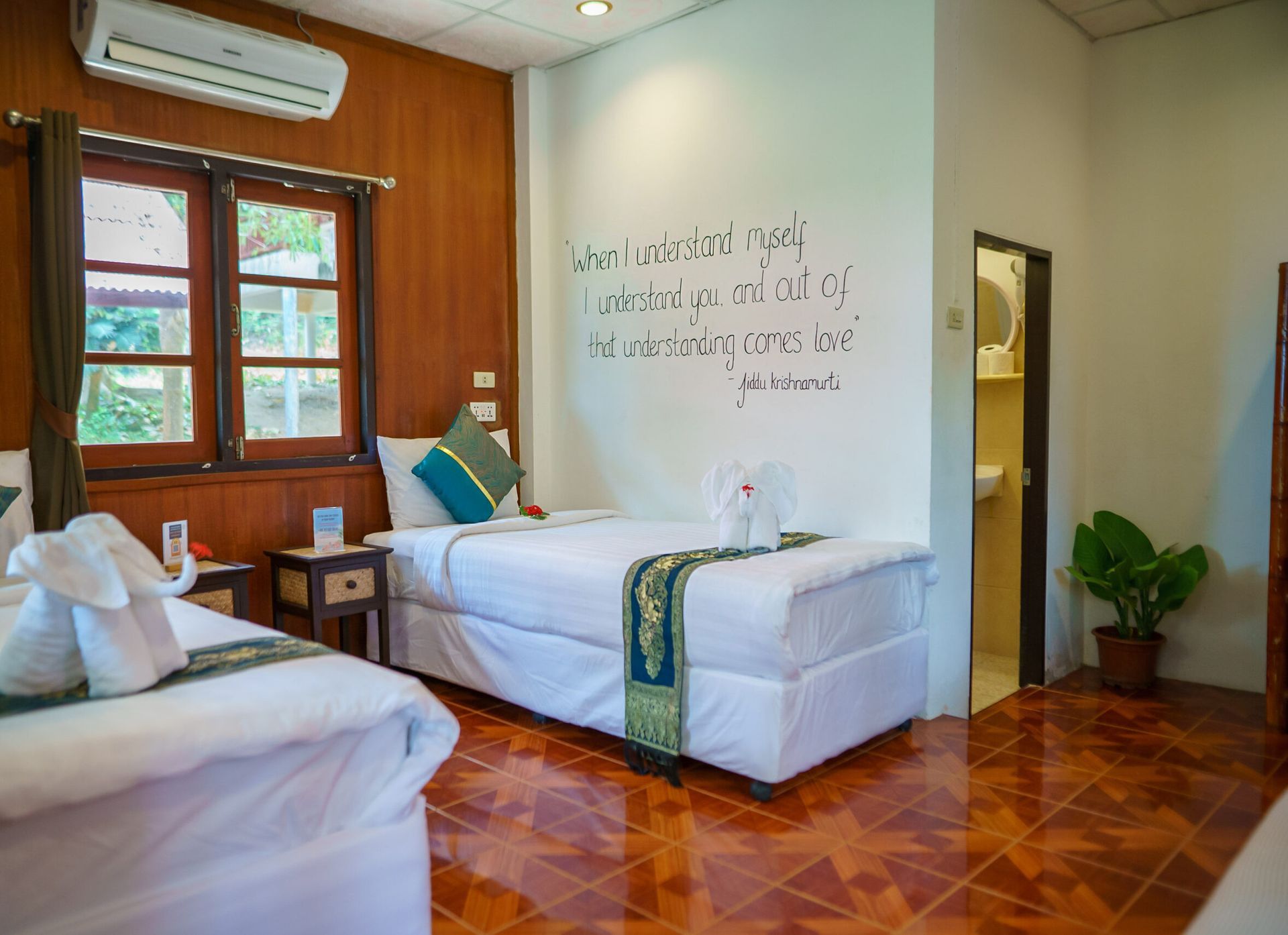 A hotel room with two twin beds, wooden walls, a bathroom, and a quote on the wall.