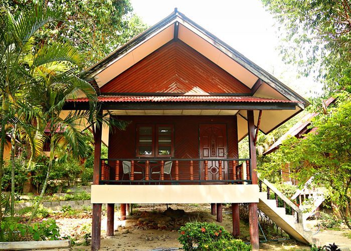 Wooden bungalow on stilts with a balcony, set in a tropical garden.
