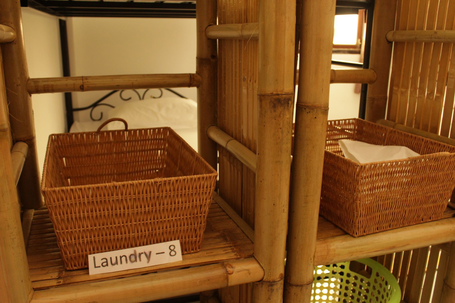 Laundry baskets on a bamboo shelf in a room, with a bed in the background.