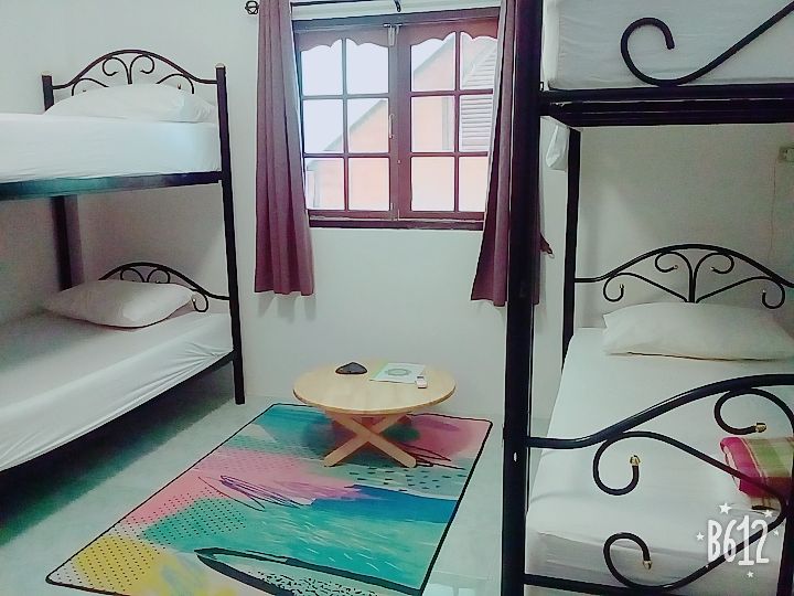 Room with two sets of bunk beds, small table, colorful rug, window with curtains.