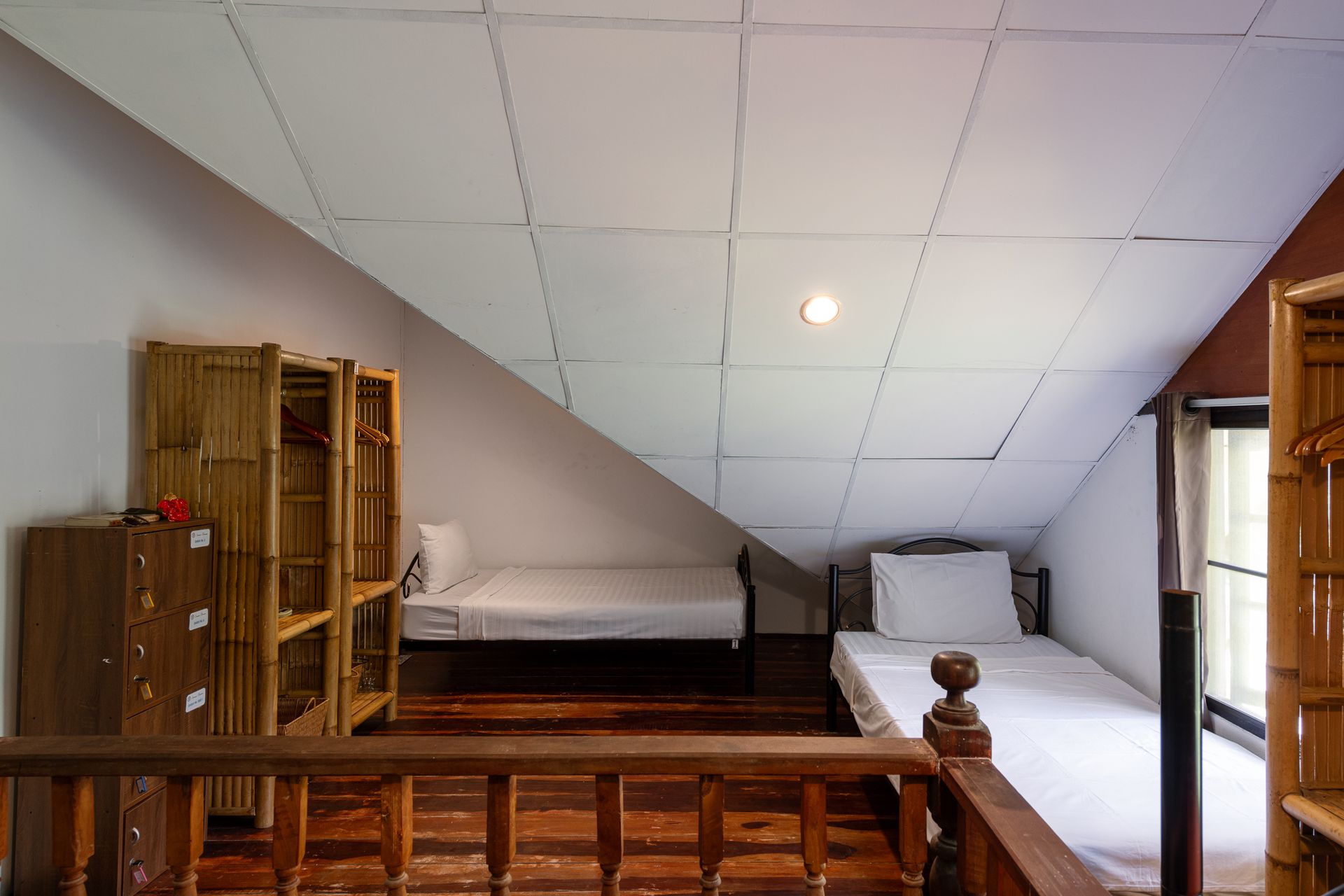 Loft bedroom with two beds, bamboo shelving, sloped ceiling, and wood railing.
