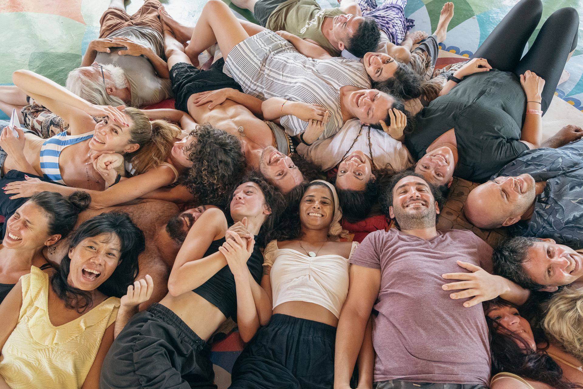 Group of diverse people lying together on a colorful surface, smiling and looking up.