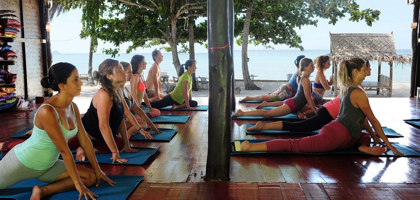 People doing yoga on mats near a beach. Some are in a Pigeon Pose.
