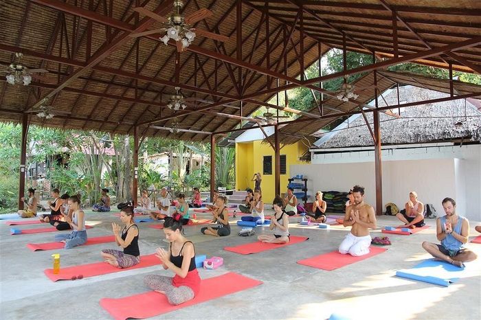People in outdoor yoga class; they sit on mats, roof overhead.