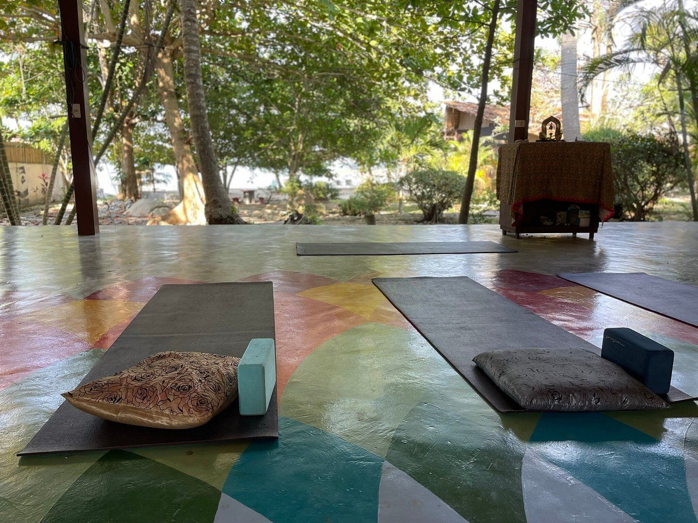 Yoga mats with props set up on a colorful, open-air platform, surrounded by trees.