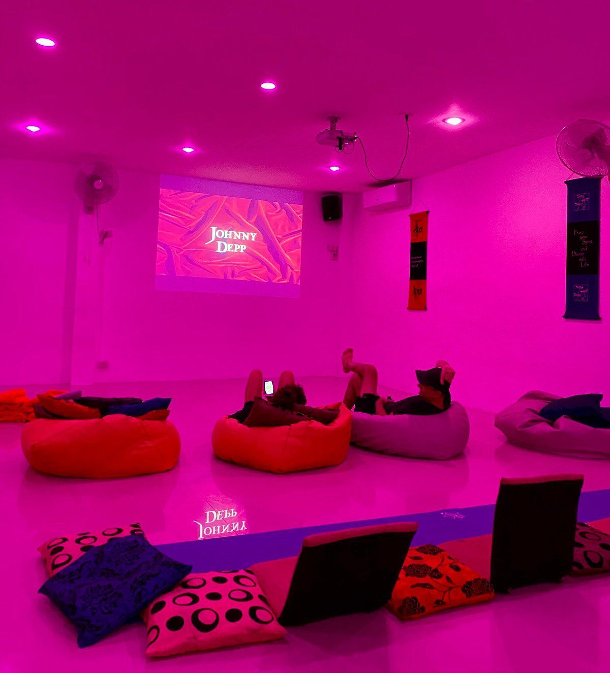 Room with people on beanbags watching a movie on a screen, lit with pink light.