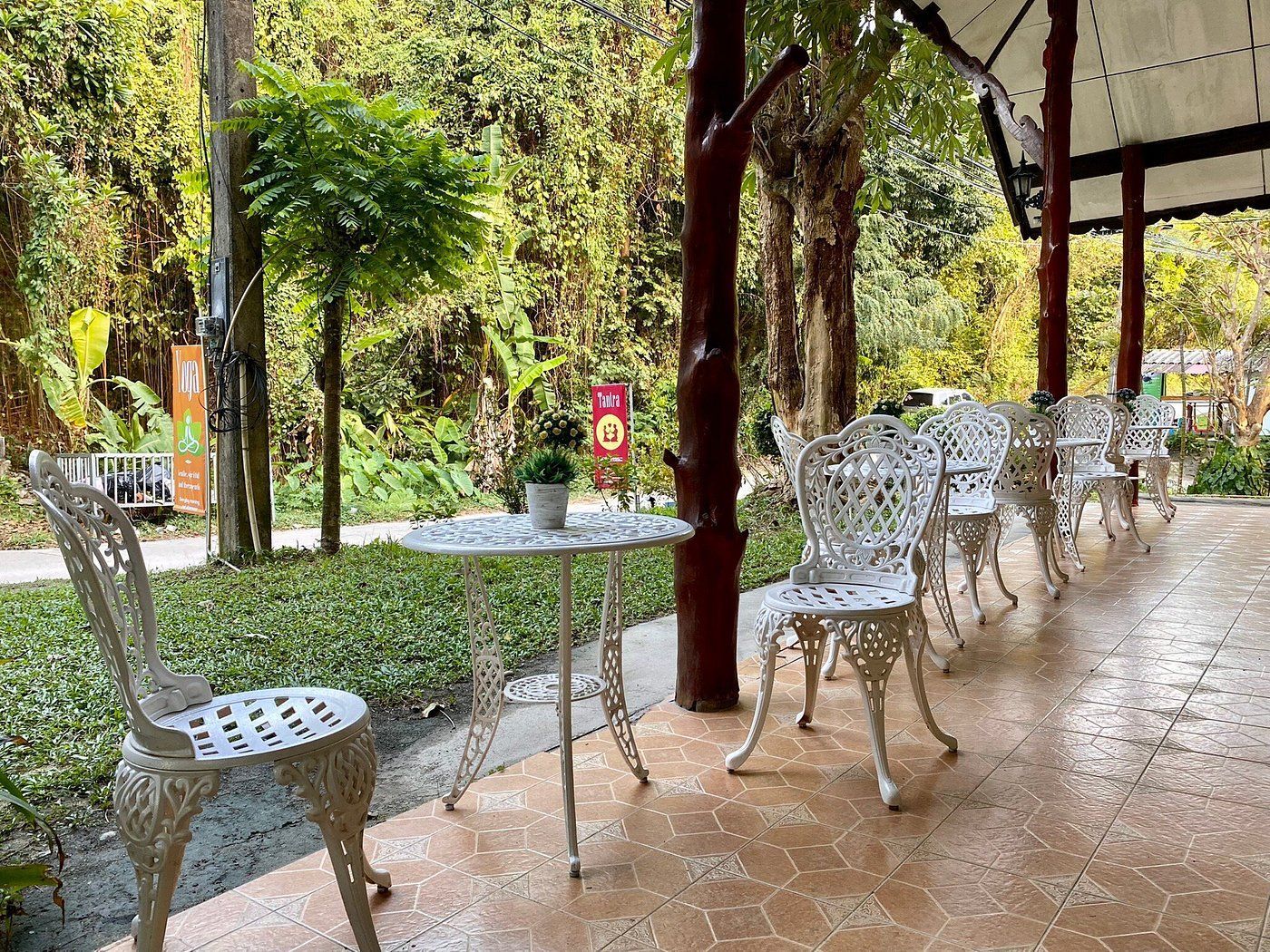 Outdoor patio with white ornate chairs and tables in a lush green garden setting.