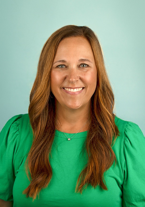 Cathy Apollos Counselor A woman in a green shirt is standing in front of a white brick wall.