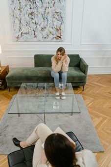 A woman is sitting on a couch talking to another woman.