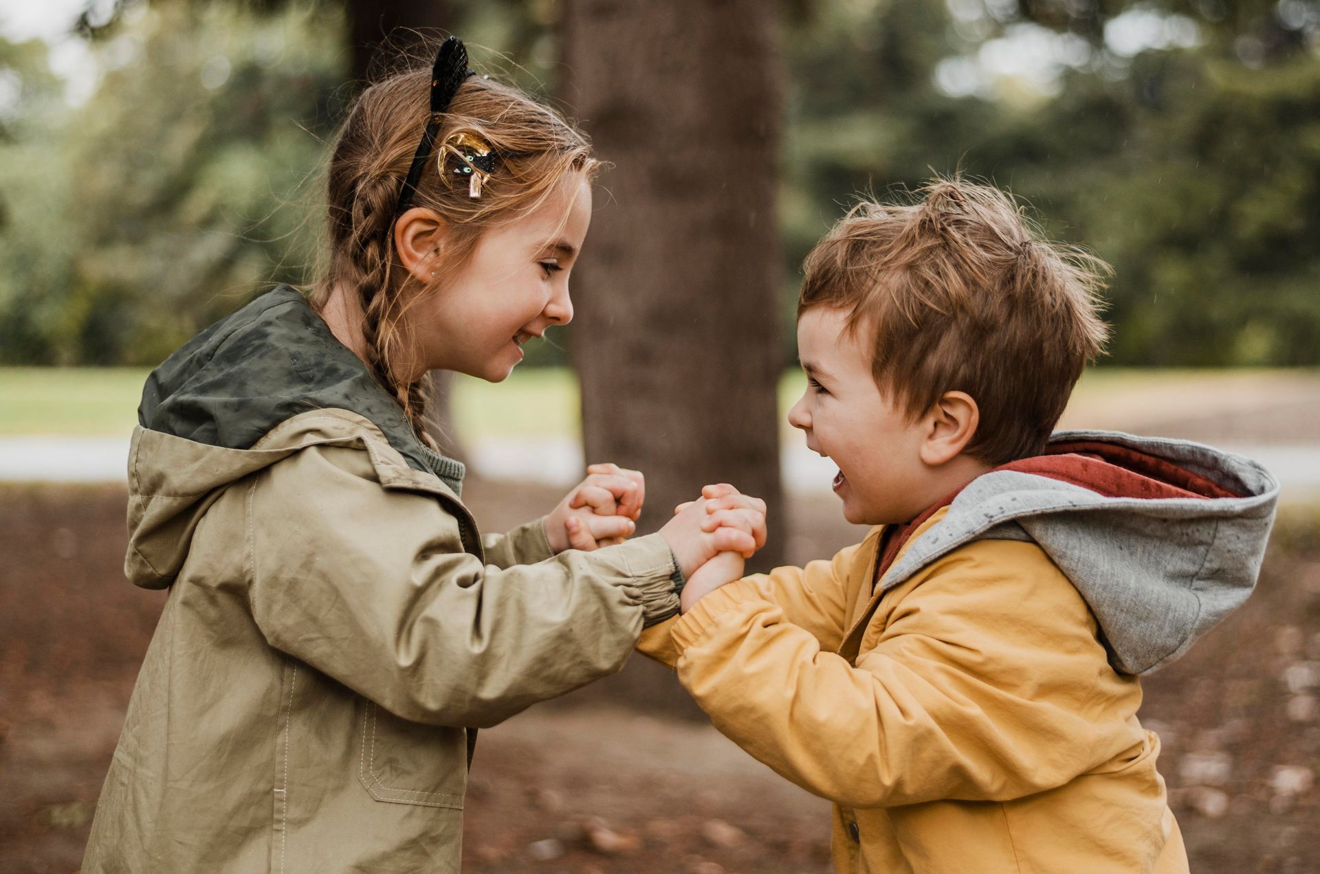 Two young children, a girl and a boy, smiling and holding hands in an outdoor