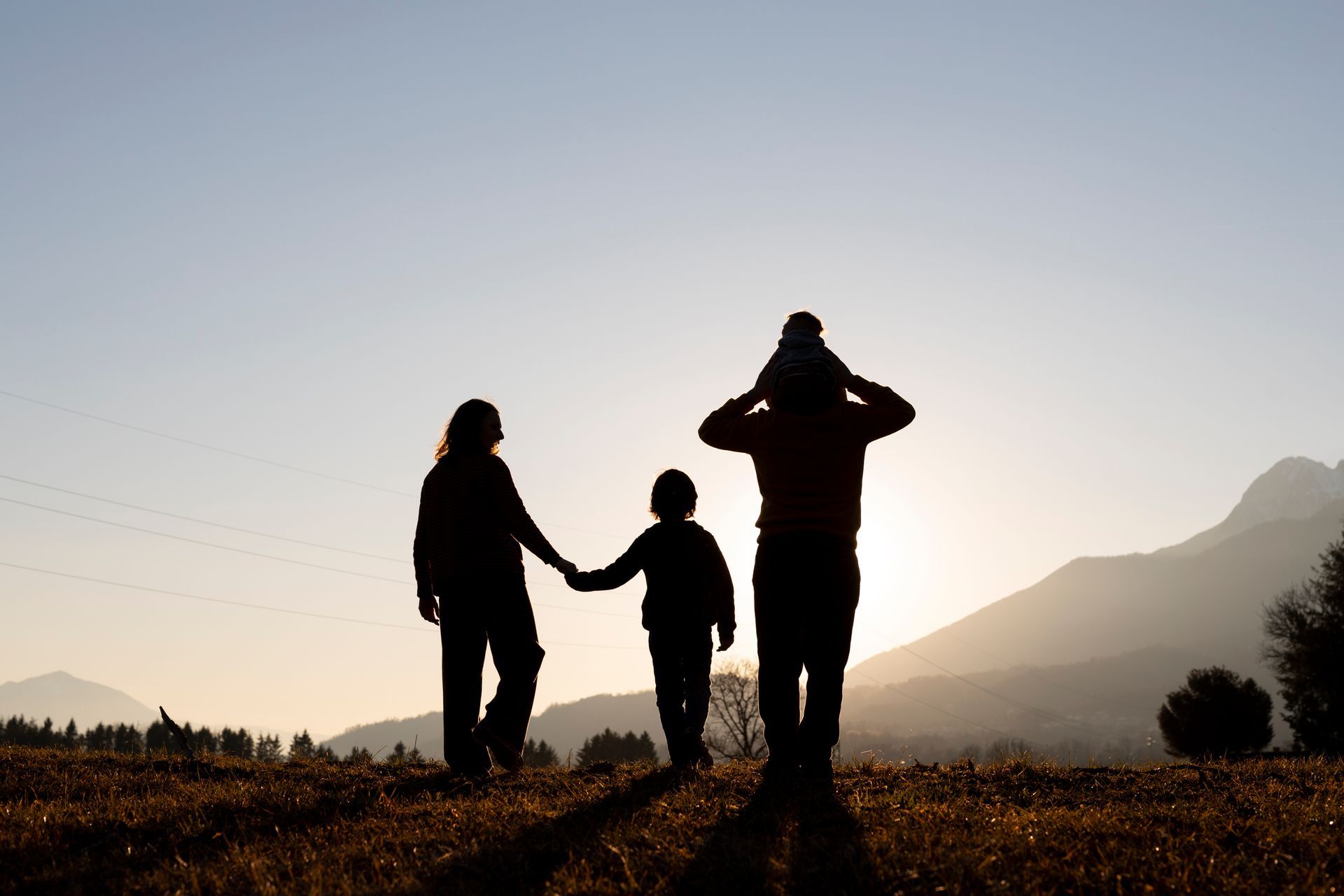 sunset; parents holding hands with a child, another child on a parent's shoulder