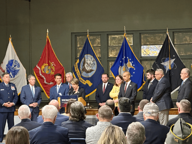 A group of people standing in front of a podium with flags in the background.