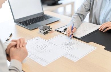 Two people are sitting at a table with papers and a laptop.