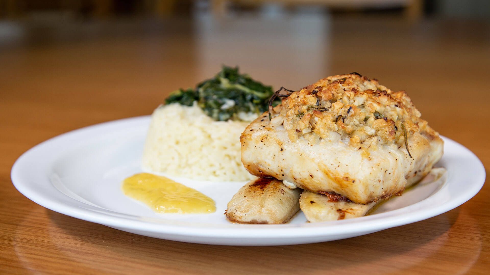 Um prato branco coberto com peixe e arroz sobre uma mesa de madeira.