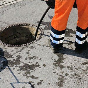 Sewerage worker on street cleaning pipe