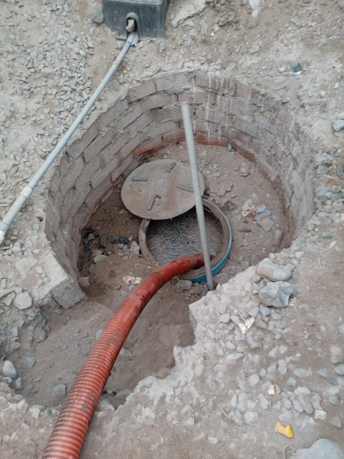 Pozo abierto en tierra con manguera en su interior y alrededor revestido de ladrillos.
