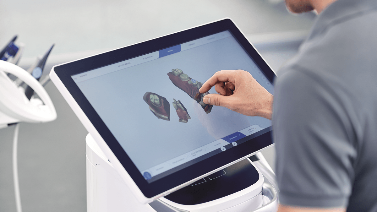 Pessoa interagindo com uma tela sensível ao toque, exibindo escaneamentos dentais em 3D.